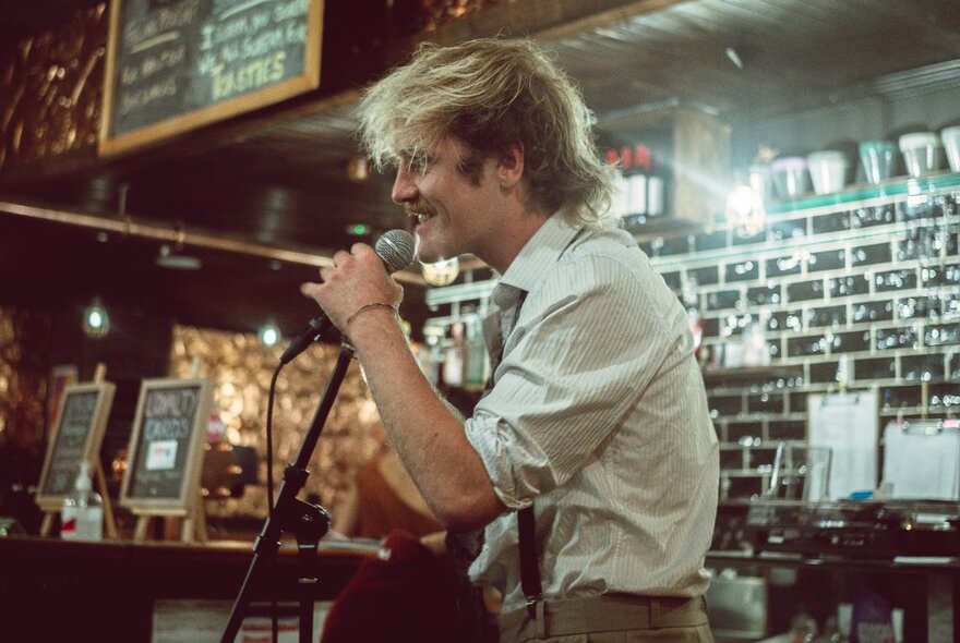 Performer standing, speaking into a microphone in a bar.