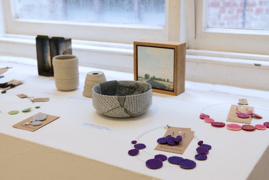 The gallery shop at fortyfivedonwnstairs, with small ceramic objects and jewellery displayed on a white counter near a window.