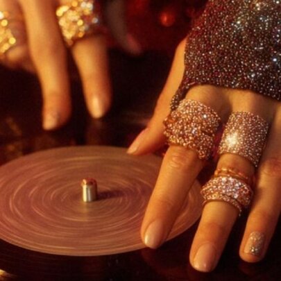 Hands with many diamanté rings on fingers handling a vinyl record. 