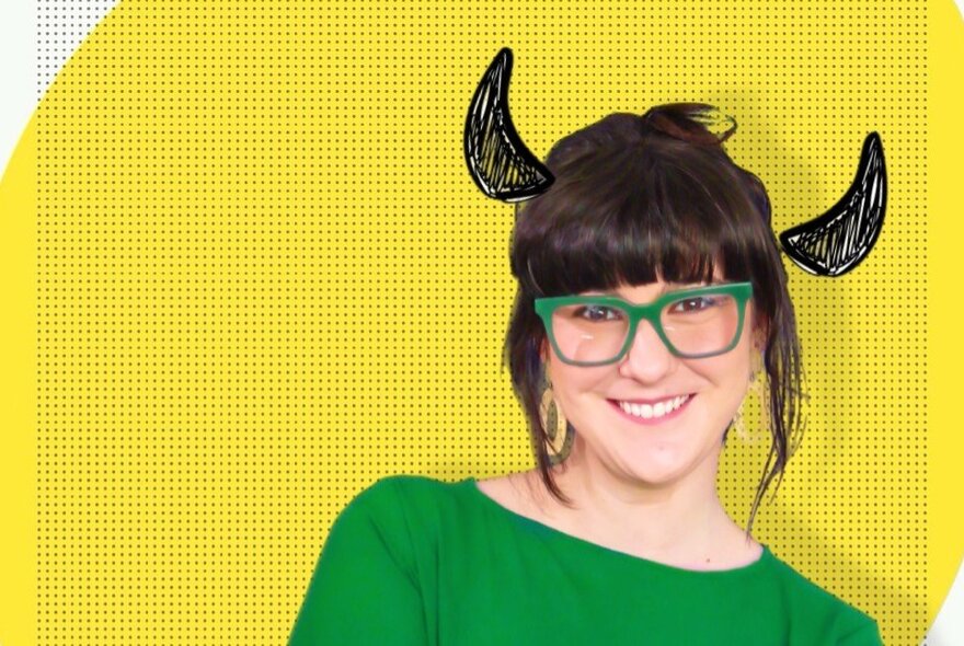 A portrait of comedian, Rebecca Perich, wearing a green top and glasses, in front of a yellow background with devil horns drawn on her head. 