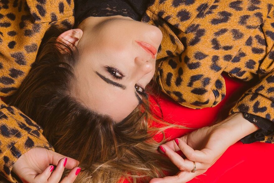 A woman lying back on a red surface, wearing a cheetah print coat.