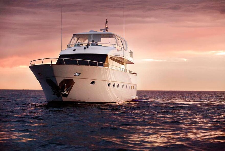 A superyacht at sea with a cloudy, sunset-tinged sky behind. 