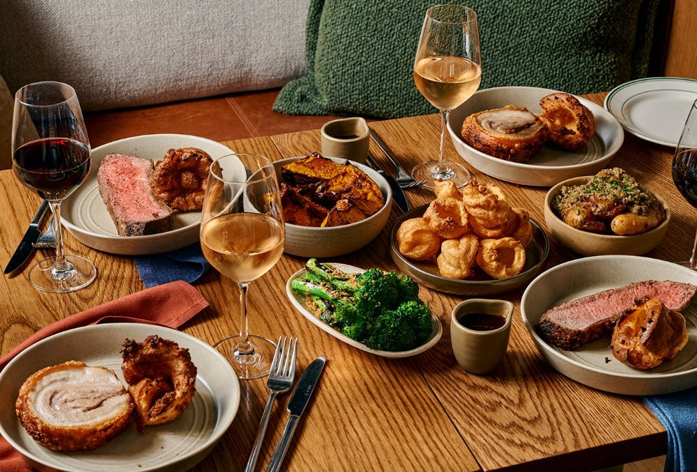 A table set with roast pork and beef, vegetables, Yorkshire puddings and wine.