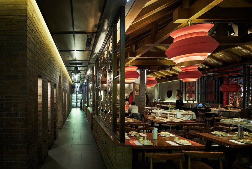 Long corridor next to restaurant interior with large red lanterns and tables set for dinner.