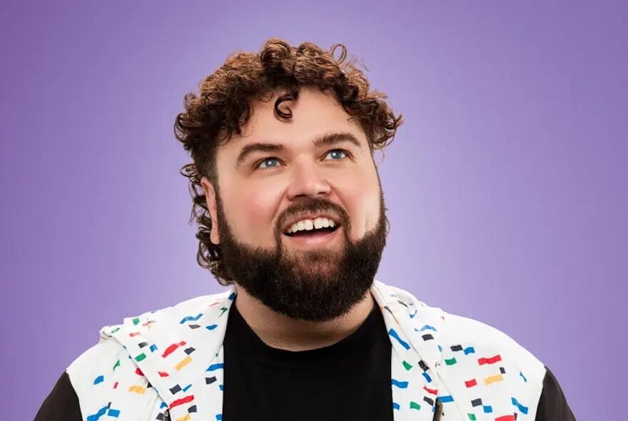Comedian Chris Demos looking upwards and smiling with an open mouth in a jacket bearing coloured sprinkles.