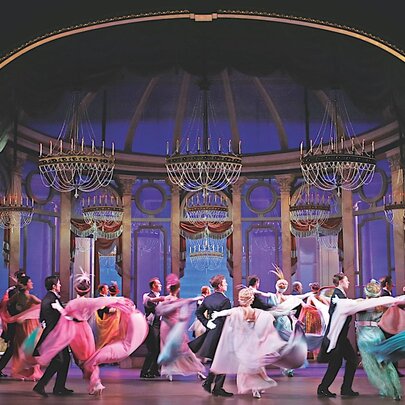A scene from a production of My Fair Lady on stage, with the cast dancing.