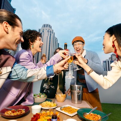 A group of friends putting their glasses together in a cheers over a table of food at an outdoor bar.