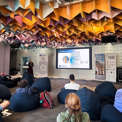 An informal presentation in a space, featuring beanbag seating and a striking geometric acoustic ceiling.