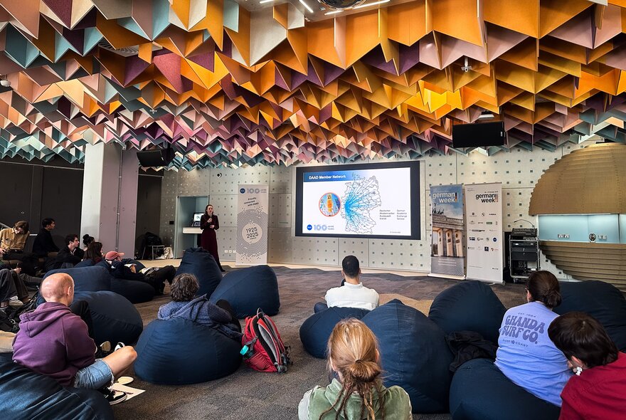 An informal presentation in a space, featuring beanbag seating and a striking geometric acoustic ceiling.