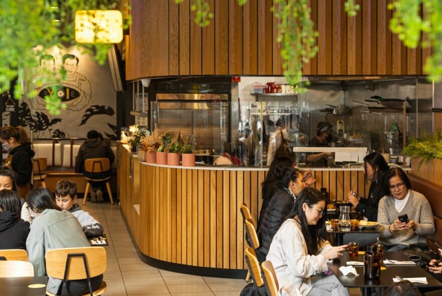 A busy restaurant with timber bar and greenery. 