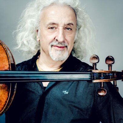 Classical musician with long curly white hair and beard, with horizontal stringed instrument.