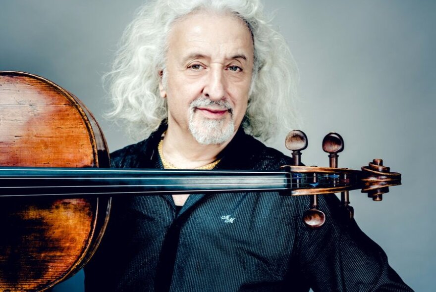 Classical musician with long curly white hair and beard, with horizontal stringed instrument.