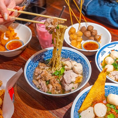 A table full of Thai food including boat noodles, skewers and fried chicken