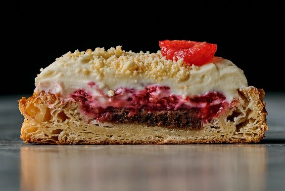 Cross section of a croissant filled with cake, raspberry jam, raspberries, and whipped white chocolate ganache.