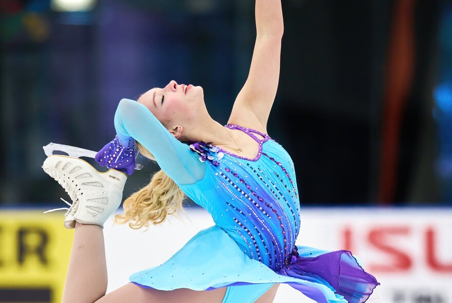 A young female figure skater holding the blade of her skate above her head as she executes a spin.