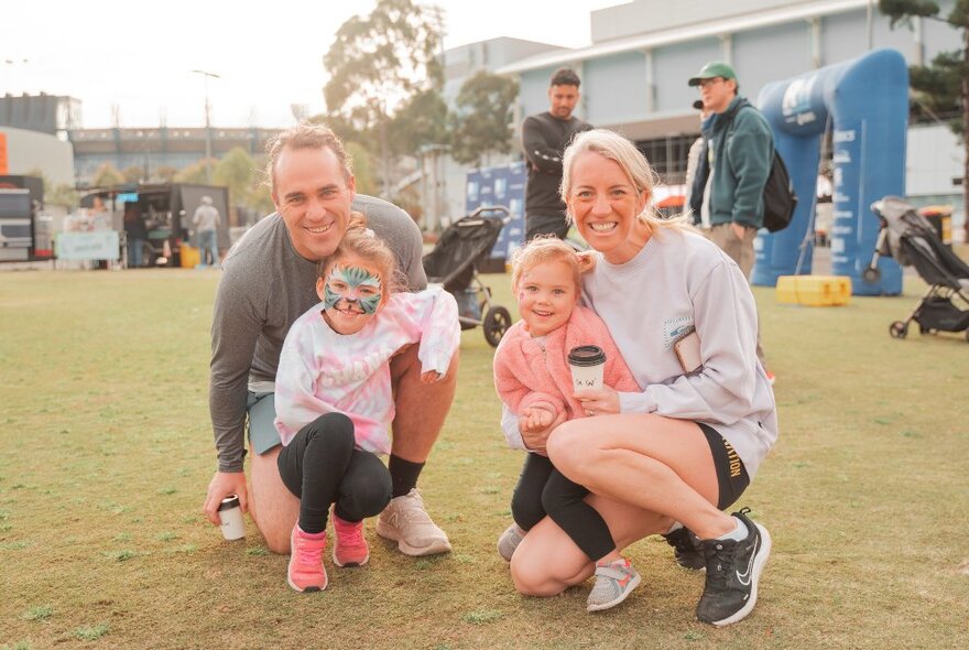 Two people kneeling down holding their kids outdoors in running gear. 