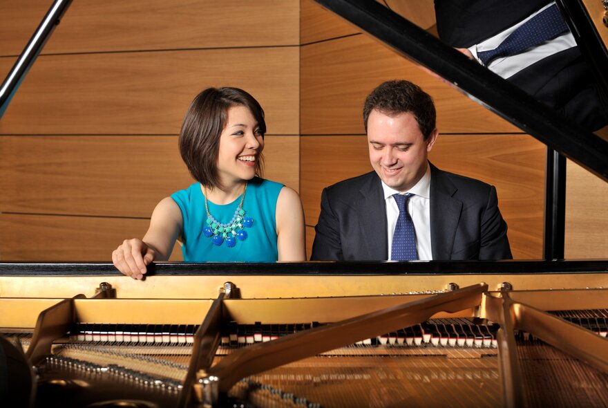 Stephanie Trick and Paolo Alderighi seated at a piano, smiling. 