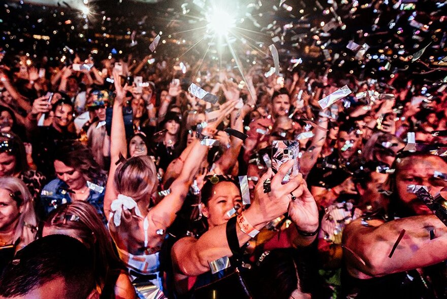 Audience with arms raised taking selfies at a concert.
