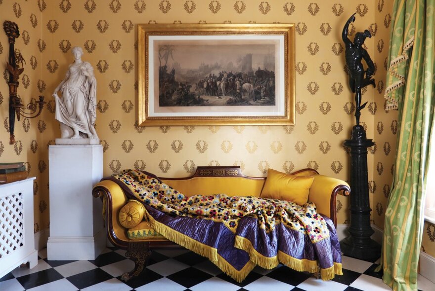 Antique sofa with draped throw in a room with wallpaper, statues and paintings.