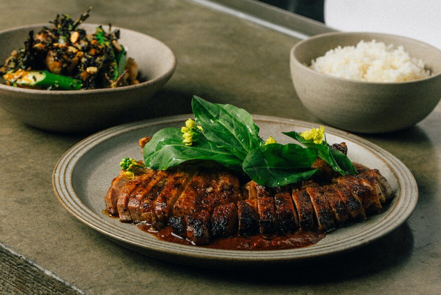 A large main with sliced meat  with a leafy garnish and a bowl of rice and another bowl. 