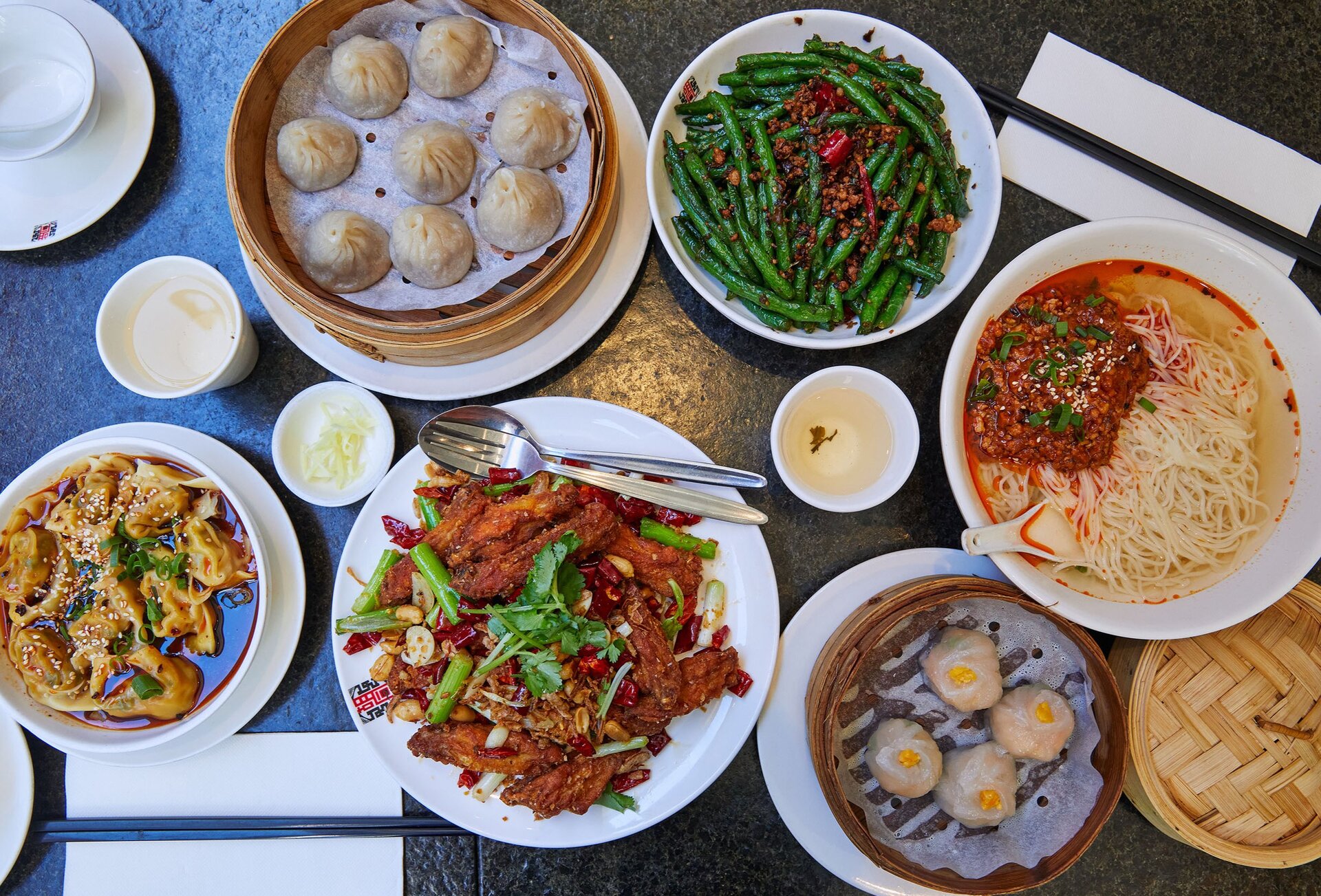 A table with plates of dumplings, noodles, beans and more Chinese dishes