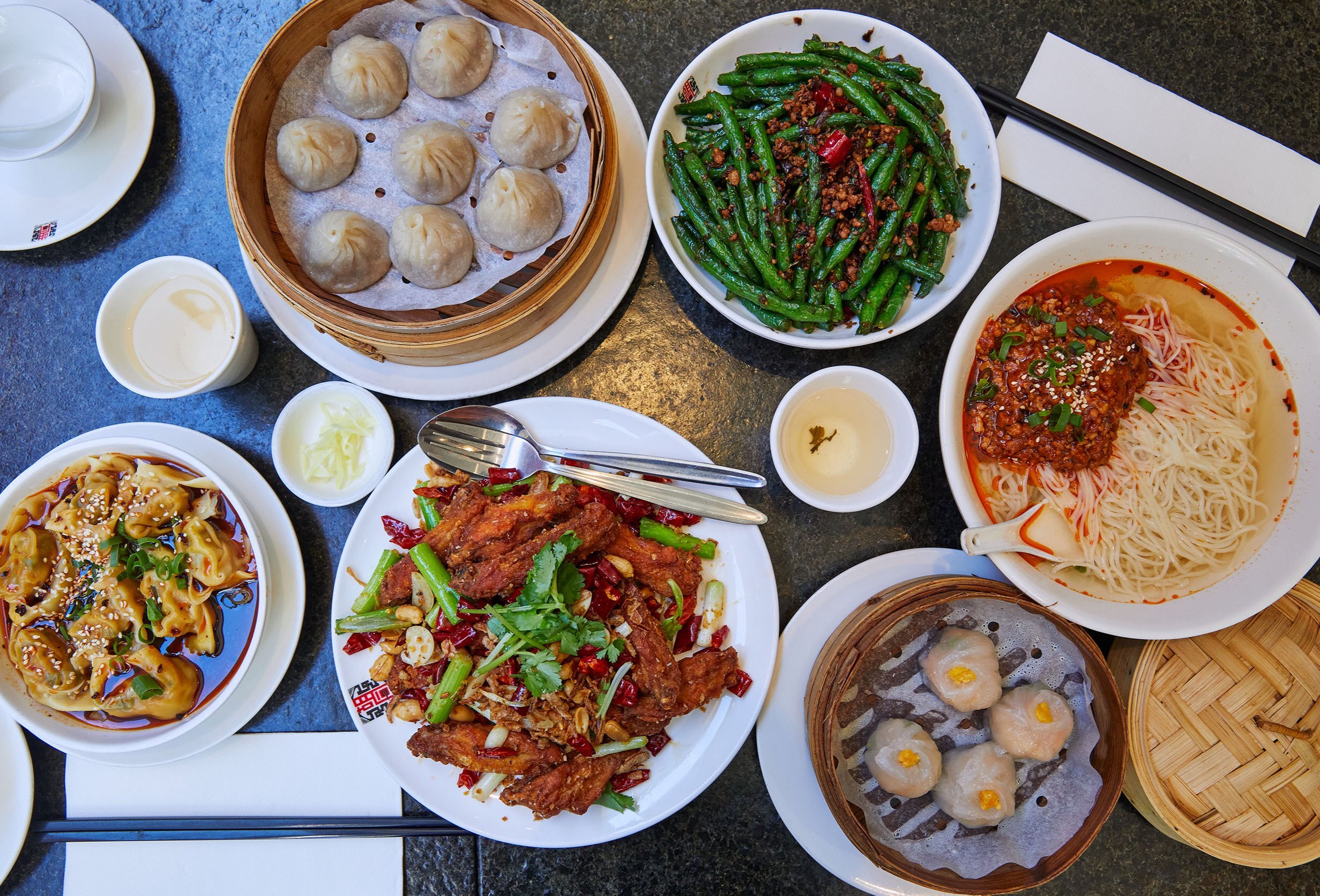 A table with plates of dumplings, noodles, beans and more Chinese dishes