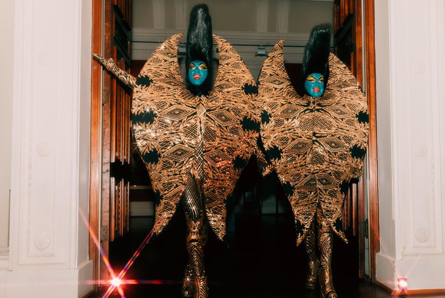 Performers dressed in flamboyant floral-inspired dress with blue make-up and bouffants.