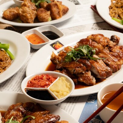 A spread of Singaporean dishes including noodles, chicken and sauces presented on white plates.