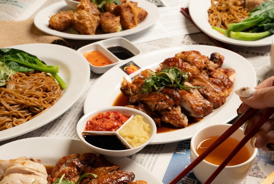 A spread of Singaporean dishes including noodles, chicken and sauces presented on white plates.