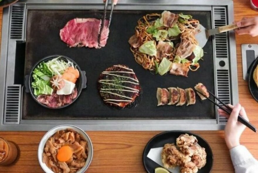 People using chopsticks to select from a range of Japanese food. 