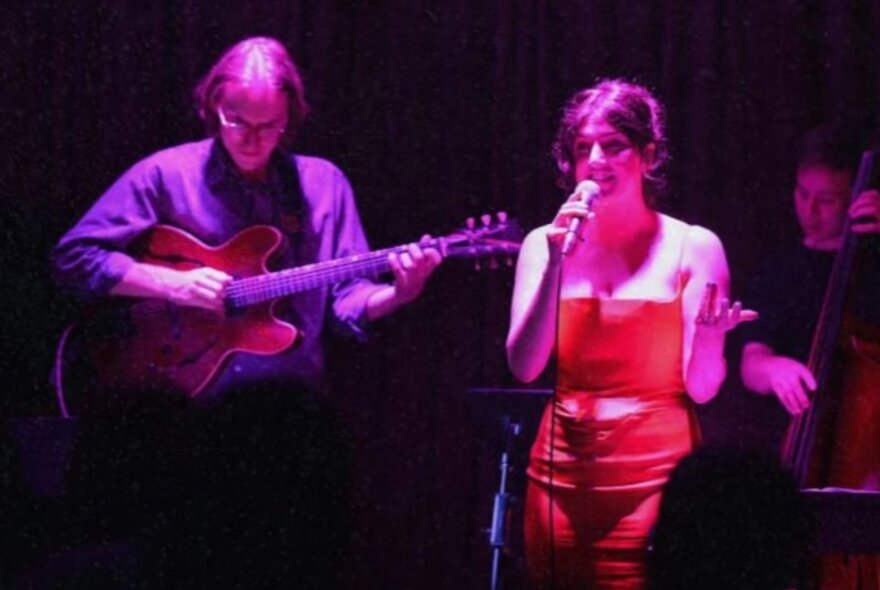 Singer, guitarist and bass player performing on stage under purple lights.
