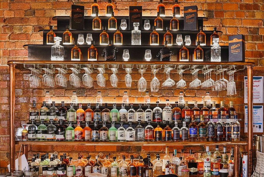 Shelves stacked with bottles and glasses against a brick wall.