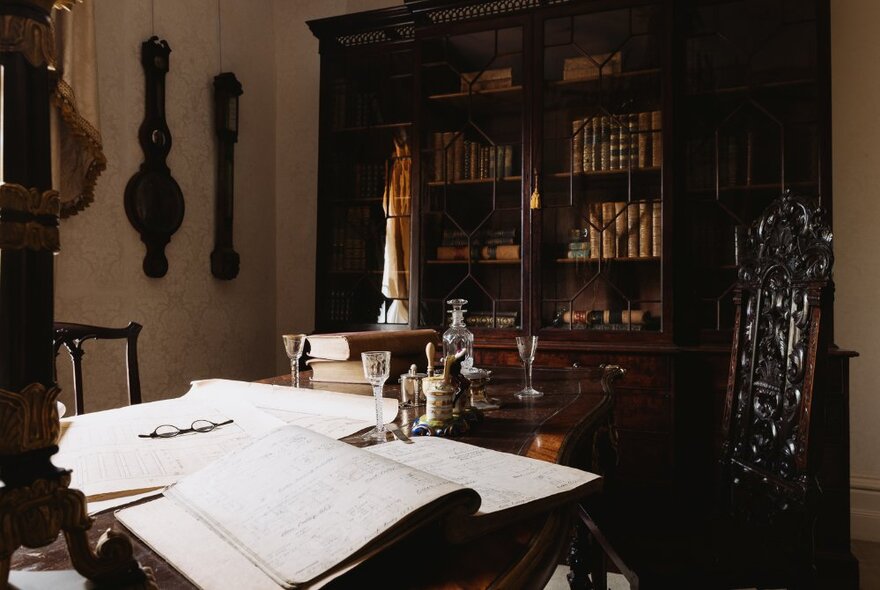 A room at The Johnson Collection Georgian mansion with a large book case against a wall, open ledgers on a writing desk, and other objects relevant to a formal study space.