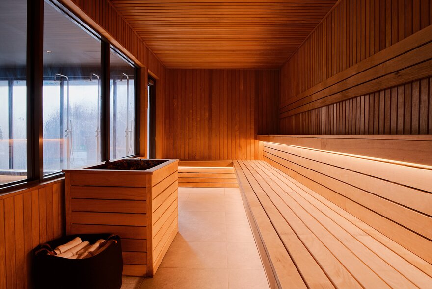 The interior of a large sauna, completely timber lined except for a glass window. 