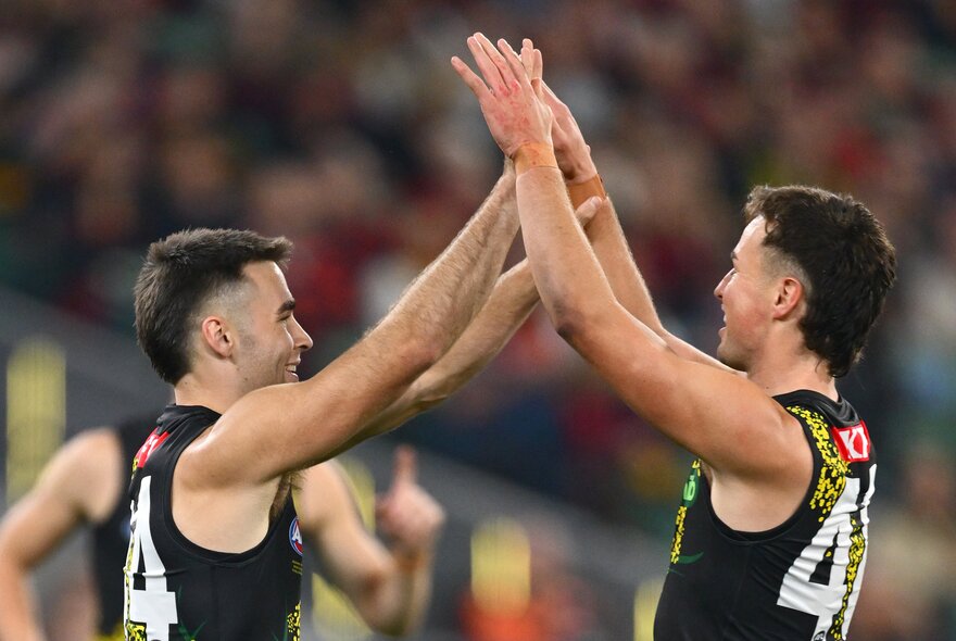 Two Richmond AFL football players high fiving each other's palms during a match.