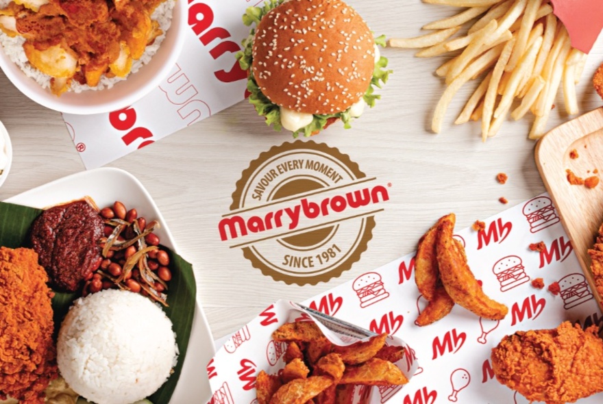 Looking down at plates of fried chicken, fries, burgers and rice on Marrybrown branded paper placemats.