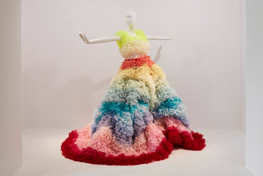 A white mannequin wearing a puffy dress made of coloured layers. 