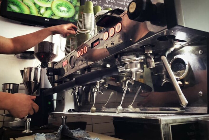 Silver coffee machine, hands to left operating.