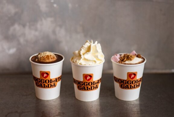 Three takeaway cups of hot chocolate, one with whipped cream.