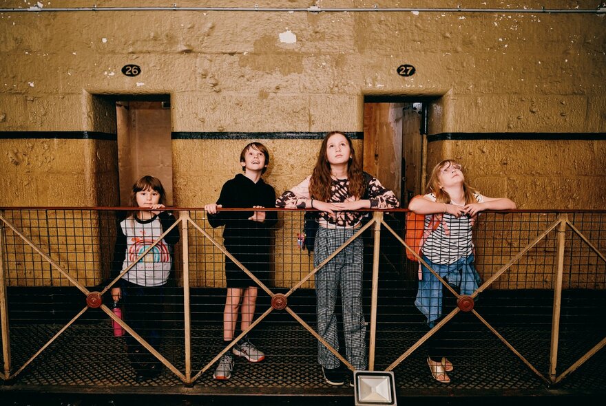 Four kids lean on the balcony inside the Old Melbourne Gaol. 