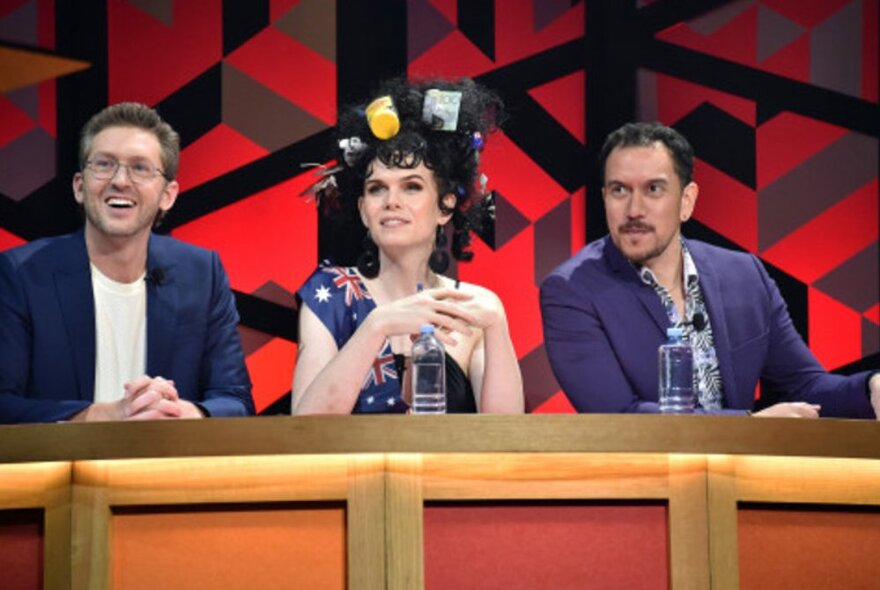 Three comedians on one side of a debating team, sitting behind a panel.