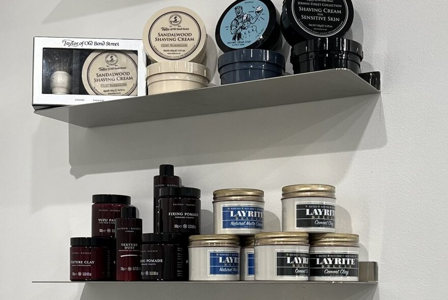 Two shelves of hair products on a white wall inside a barber shop.