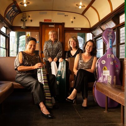 The four members of the Flinders Quartet seated with their instruments in cases beside them, inside a stationary vintage W class Melbourne tram.