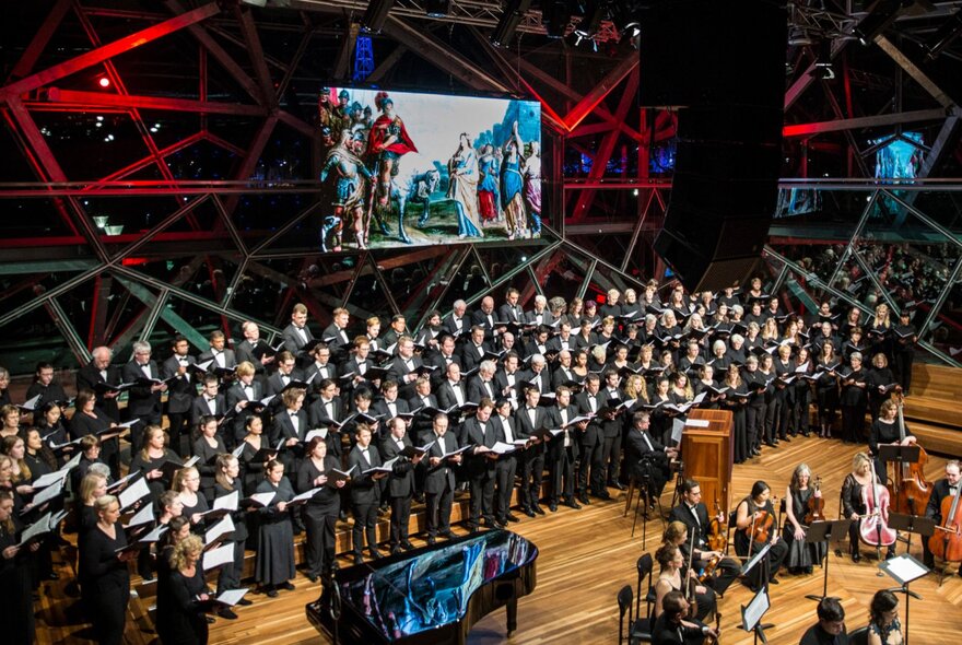 Massed choir on stage in front of a large screen.