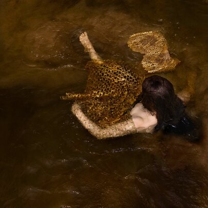 Art photograph of a female floating on water viewed from above.