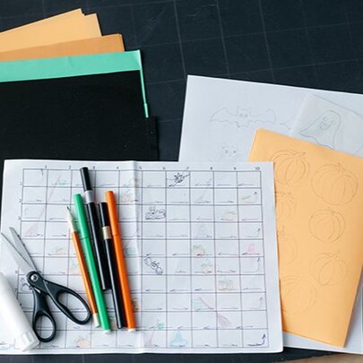 A collection of coloured paper and pens with scissors and glue, and a home-made board game board.
