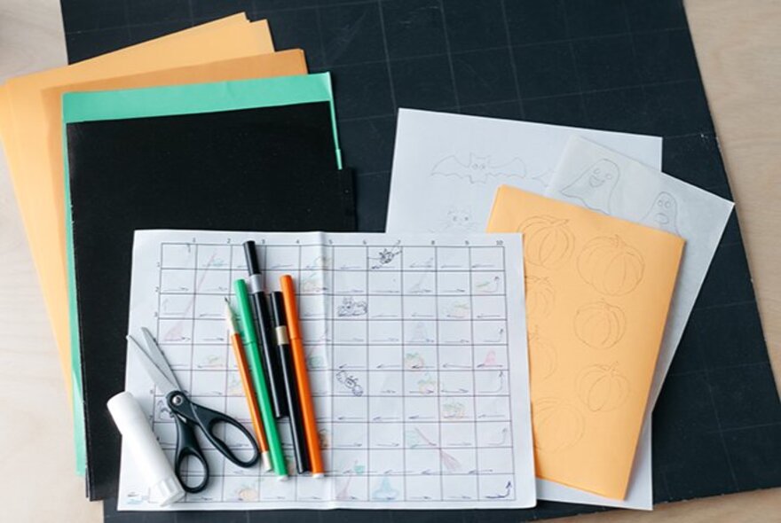 A collection of coloured paper and pens with scissors and glue, and a home-made board game board.