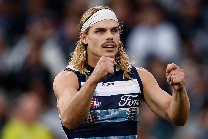 Geelong AFL football player with arms in front of him and fists clenched during a match.