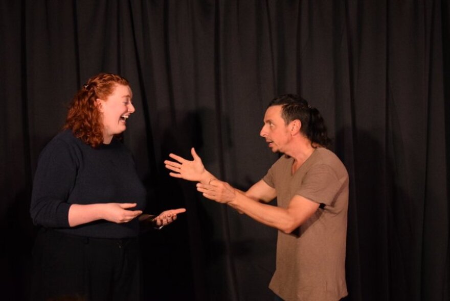 Two actors improvising on a stage in front of an black curtain.