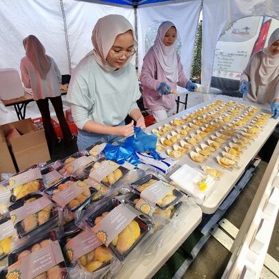 Four women behind tables of food produce, in a marquee. 